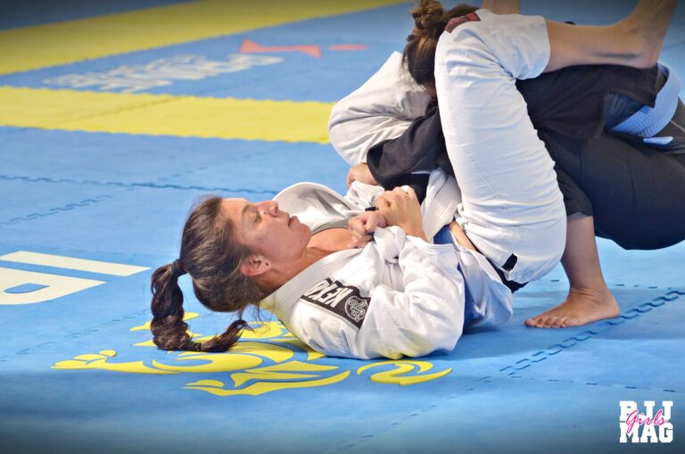 Lutadora de jiu-jitsu faixa branca segurando uma faixa azul no tatame