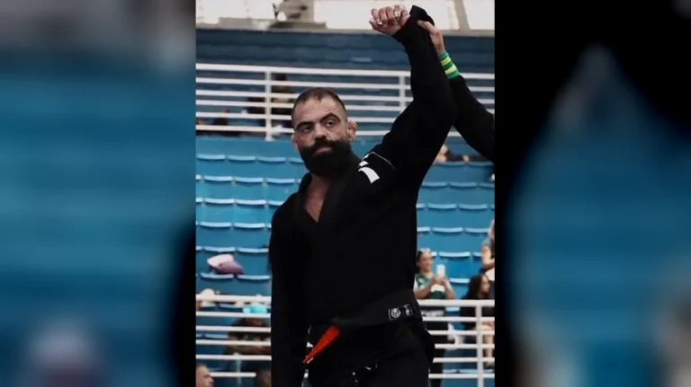 Matheus Knorr, professor de jiu-jitsu da Aspira BJJ, de kimono preto com o braço erguido em campeonato